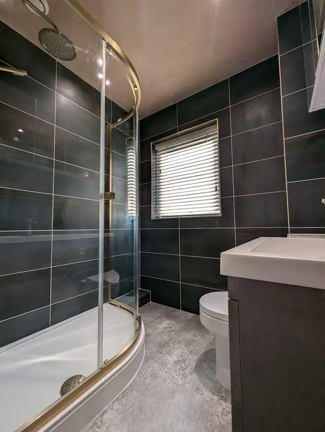 Bathroom with dark grey wall tiles, curved glass shower screen and wall hung vanity