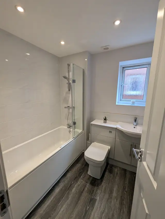 White bathroom with bath, shower screen and dark wood effect floor