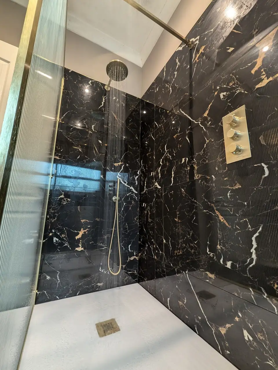 Walk in shower with black and gold marble effect tiles and brushed brass fittings, fitted by JTT Property Services near Norwich
