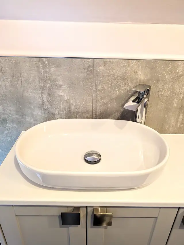 Oval countertop basin on a grey vanity with tiled splashback